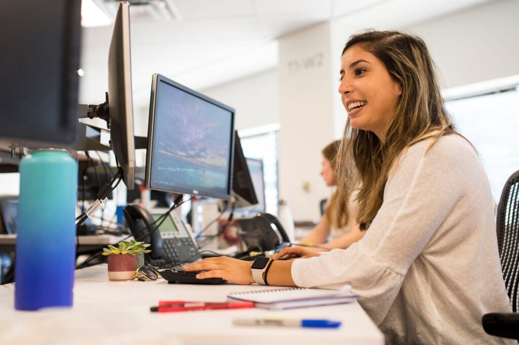 Smiling student looks at monitor and types at workstation